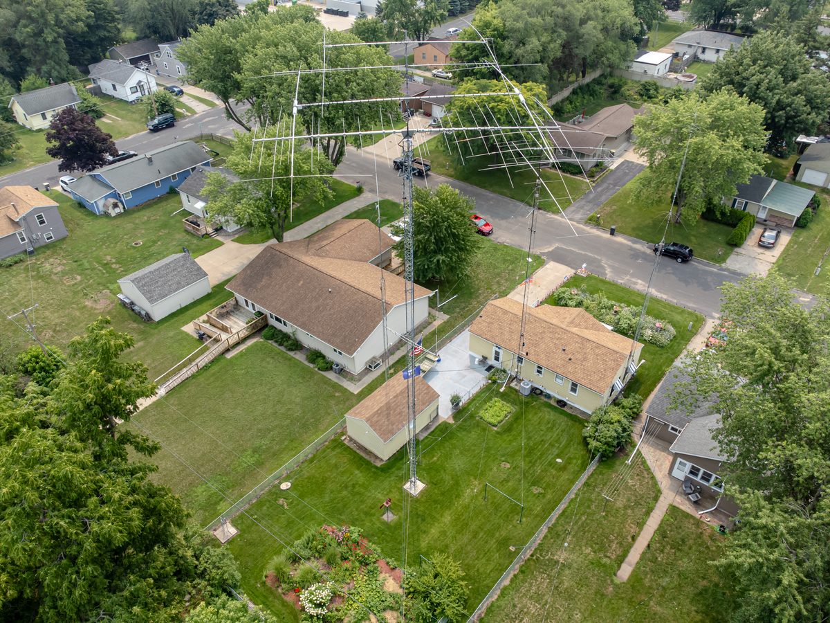 Luftaufnahme einer Wohnsiedlung mit einem Gittermast im Garten, auf dem mehrere große Richtantennen montiert sind