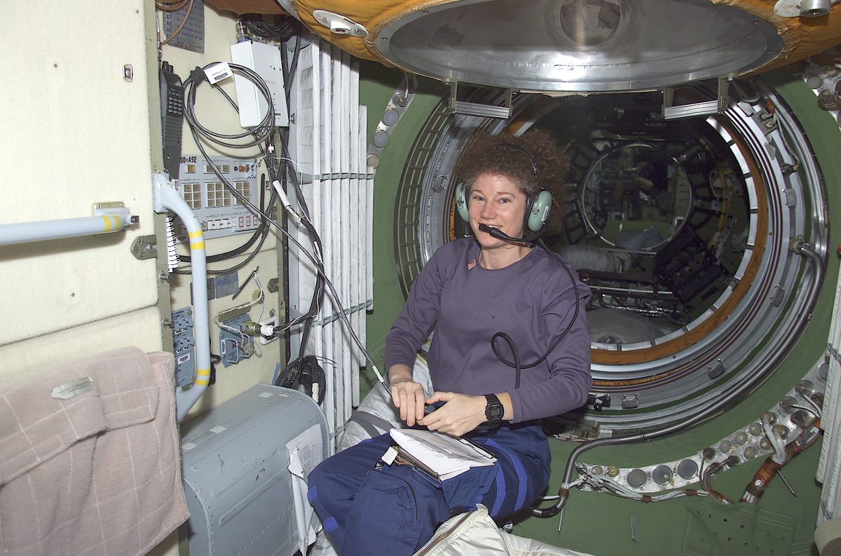 Astronautin Susan Helms mit Kopfhörer und Mikrofon an der Amateurfunkstation im Sarja-Modul der ISS, hinter ihr die runde Luke zum nächsten Modul