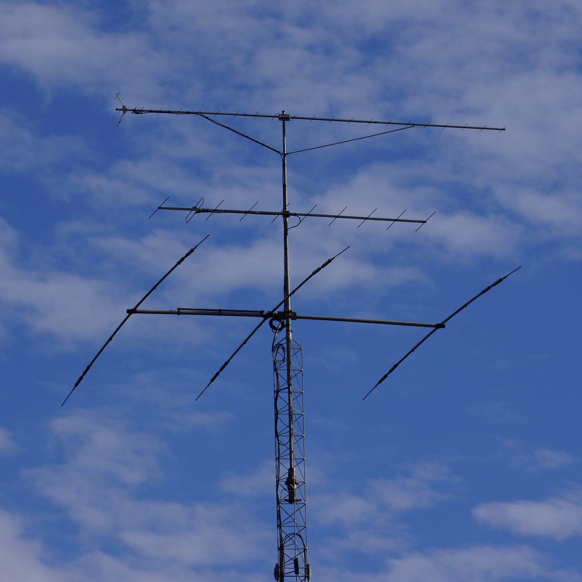 Gittermast vor blauem Himmel mit drei übereinander montierten Richtantennen, unten eine große Kurzwellen-Yagi, darüber zwei lange UKW-Antennen