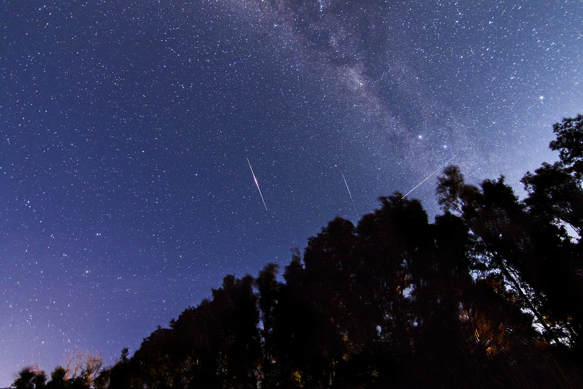Sternenhimmel mit Milchstraße, zwei helle, spindelförmige Lichtstriche von Iridium-Flares und die dünne Spur der ISS