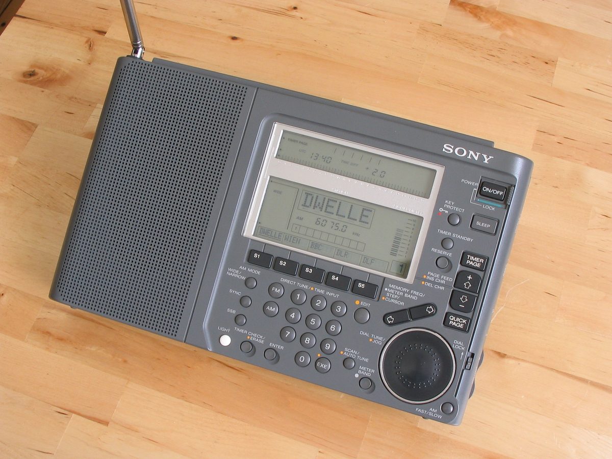 Grauer Weltempfänger Sony ICF-SW77 mit ausgezogener Teleskopantenne, Zifferntastatur und Abstimmrad, im Display der Sendername DWELLE